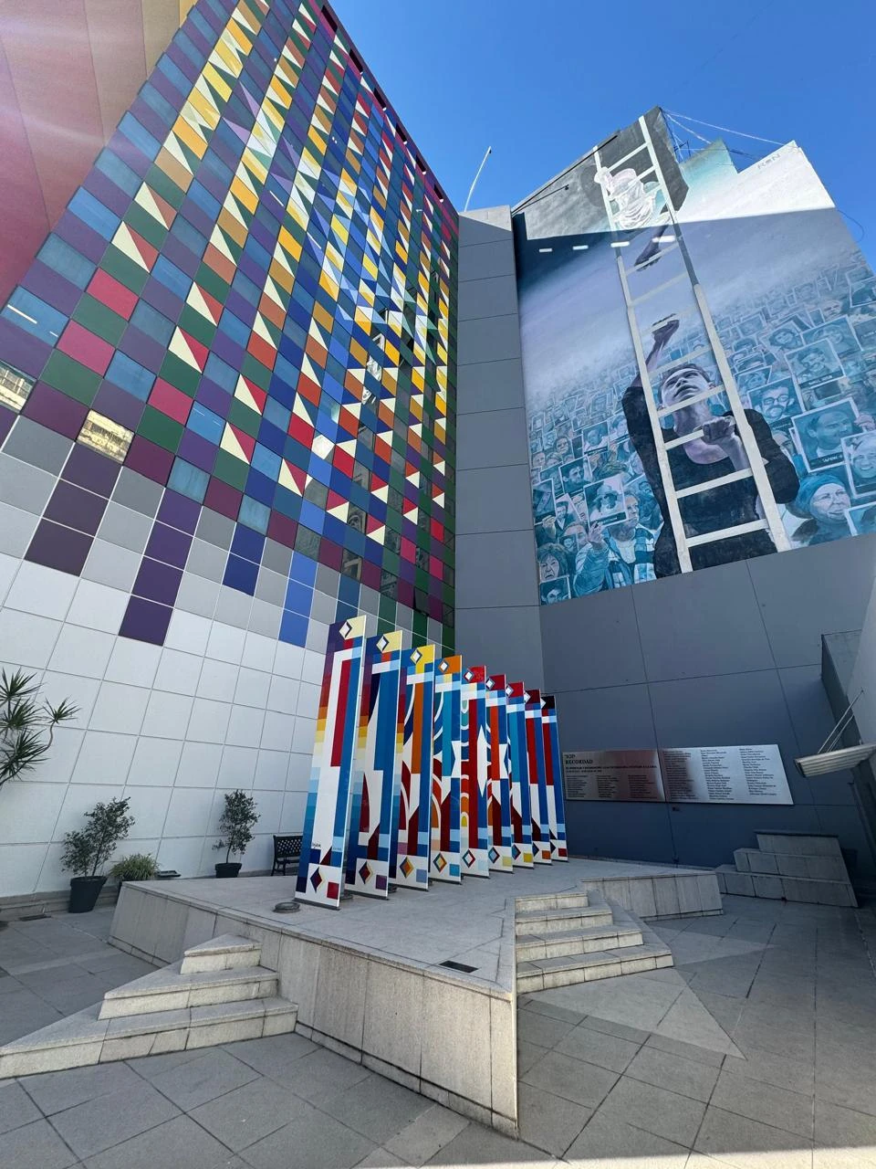 Interior courtyard of the AMIA Jewish Center in Buenos Aires with colorful commemorative murals, geometric painted sculptures, and a large mural with portraits of the victims of the 1994 bombing.